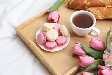 Tasty breakfast served in bed. Delicious macarons, tea, baguette and flowers on tray