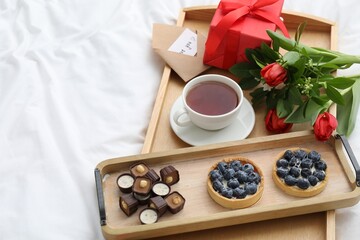 Tasty breakfast served in bed. Delicious desserts, tea, flowers and gift box on tray, space for text