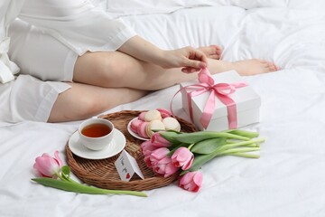 Tasty breakfast served in bed. Woman with gift box, tea, macarons, flowers and I Love You card at home, closeup