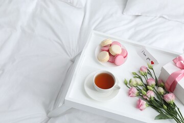 Tasty breakfast served in bed. Delicious macarons, tea, gift box, flowers and I Love You card on tray, space for text