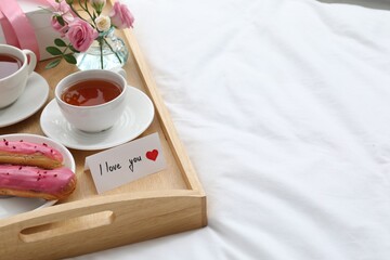 Tasty breakfast served in bed. Delicious eclairs, tea, gift box, flowers and card with phrase I Love You on tray, space for text