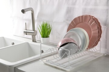 Drainer with different clean dishware on white table in kitchen