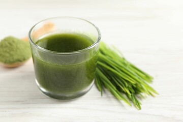 Wheat grass drink in glass and fresh sprouts on white wooden table, closeup