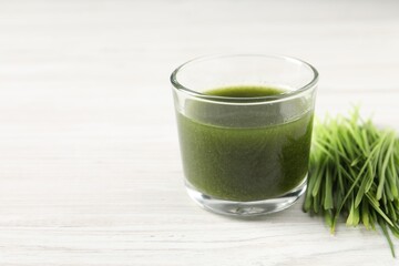 Wheat grass drink in glass and fresh sprouts on white wooden table, closeup. Space for text