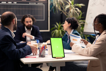 Chief executive officer hosts meeting with his staff next to mockup display, discussing latest business achievements and performance metrics. Workers share project updates or insight.