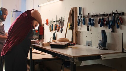 Woodworker in assembly shop using power drill to create holes for dowels in wooden board. Carpenter...