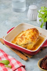 Baked chicken fillet stuffed with spinach, cheese and sun-dried tomatoes in a red baking dish on a gray concrete background. Spinach recipes.
