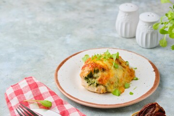 Baked chicken fillet stuffed with spinach, cheese and sun-dried tomatoes on a ceramic plate on a gray concrete background. Spinach recipes.