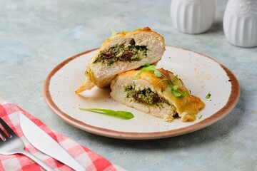 Sliced baked chicken fillet stuffed with spinach, cheese and sun-dried tomatoes on a ceramic plate on a gray concrete background. Spinach recipes.