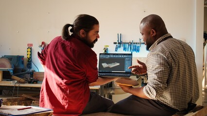 African american manufacturer and colleague comparing wood art piece with schematic displayed on...