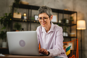 Mature woman with eyeglasses work from home on laptop smile positive