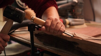 Craftsperson carving into wood using chisel and hammer in carpentry shop with precision....