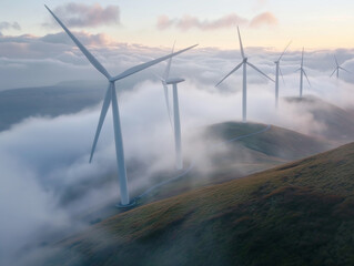 Fototapeta premium Majestic wind turbines rise above cloud-covered hills at dawn, harnessing wind energy in a tranquil landscape.