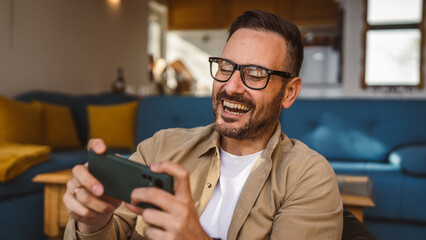 Adult man with eyeglasses play video games on his phone at home