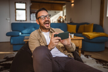 Adult man with eyeglasses play video games on his phone at home