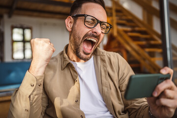 Adult man with eyeglasses play video games on his phone at home