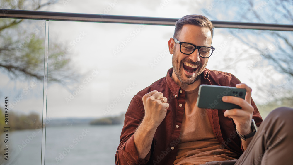 Wall mural adult man with eyeglasses play video games on his phone at home