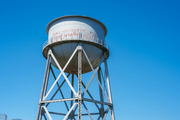 Tall white water tower with conical top, metal lattice beams, PEACE AND FREEDOM WELCOME HOME OF THE FREE INDIAN LAND message. Location Alcatraz Island, San Francisco, USA.