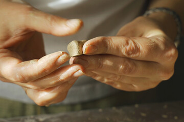 A woman potter twists a small piece of clay with her palms.