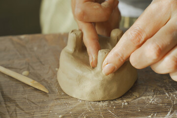 The woman shapes the product and cuts off excess clay from the legs of the pot.