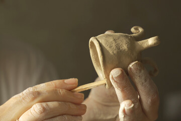 A woman potter decorates a clay product with patterns using a tool.