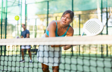 Young woman in skirt playing padel tennis on court. Racket sport training outdoors.