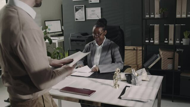 Back tracking footage of male client with documents coming to consultation to female attorney and greeting with handshake in modern office