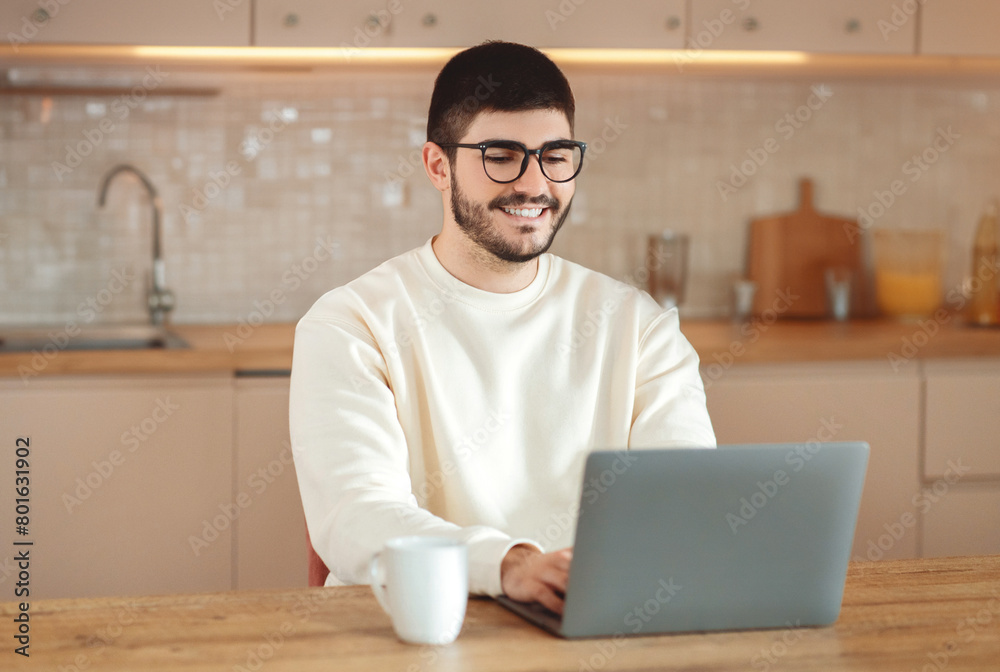 Aufkleber A man is seated at a table, focused on working with a laptop computer in front of him. His hands are typing on the keyboard as he stares at the screen, seemingly engaged in the task at hand.