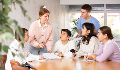 Smiling motivated young female team leader holding meeting with group of fellow students,...