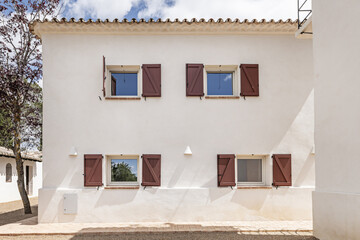 White facades of a country house with windows with red wooden shutters and terracotta and gravel floors
