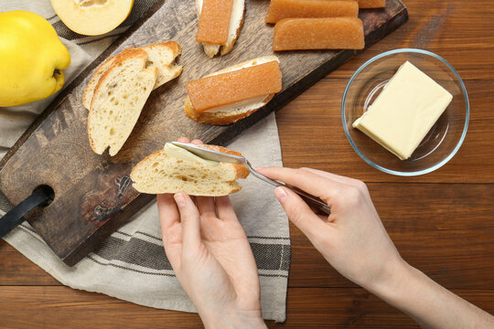 Making sandwich with quince paste. Woman buttering bread at wooden table, top view