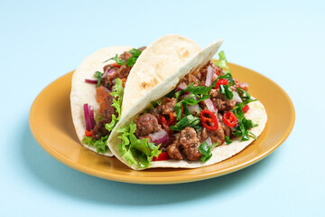 Delicious tacos with meat and vegetables on light blue table, closeup