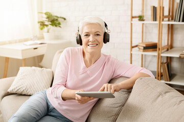 Senior woman enjoying music and watching videos on tablet pc in headphones, free space