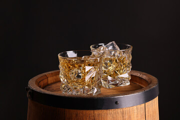 Whiskey in glasses on wooden barrel against dark background
