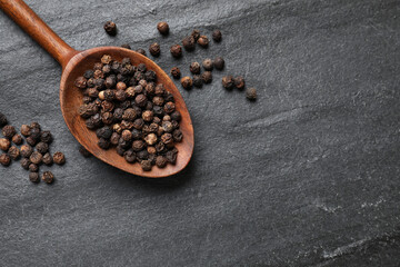 Aromatic spice. Pepper in spoon on black table, top view. Space for text