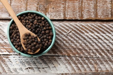 Aromatic spice. Black pepper in bowl and spoon on wooden table, top view. Space for text