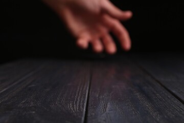 Man holding hand above black wooden table, selective focus. Space for text