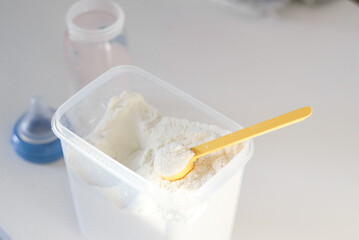 Dry powder formula milk for feeding babies in a can with yellow plastic scoop and empty feeding bottle