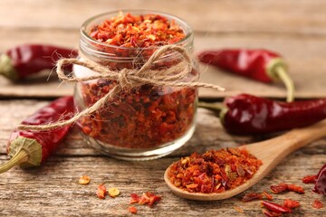 Chili pepper flakes and pods on wooden table, closeup