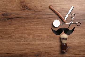 Artificial moustache and barber tools on wooden table, flat lay. Space for text