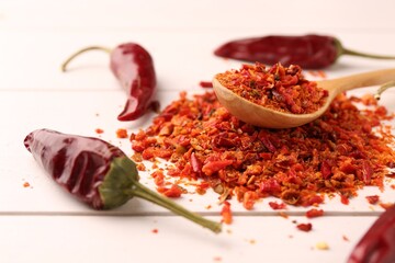 Chili pepper flakes and pods on white wooden table, closeup