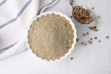 Ground pepper and peppercorns on white tiled table, top view