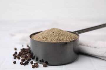 Ground pepper and peppercorns on white tiled table, closeup