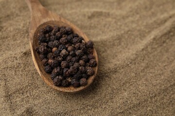Aromatic spice. Spoon with peppercorns on ground black pepper, closeup