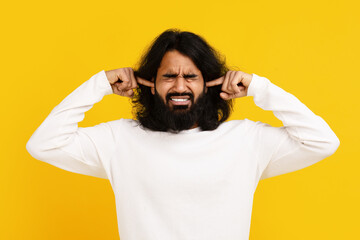 Indian man with long hair and a beard is shown holding his hands on his ears, indicating a gesture...