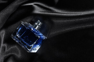 Luxury men's perfume in bottle on black satin fabric, above view. Space for text