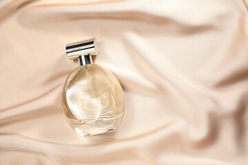 Luxury perfume in bottle on beige silk fabric, top view