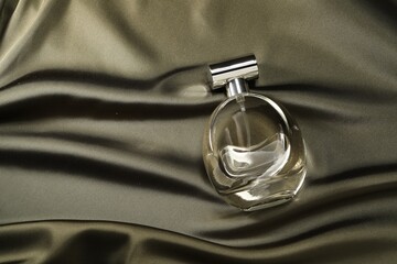 Luxury perfume in bottle on dark silk fabric, top view