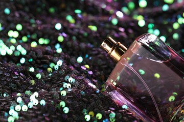 Luxury perfume in bottle on fabric with colorful sequins, closeup