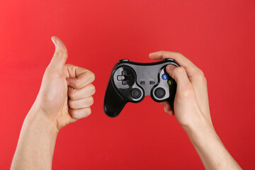 Man using wireless game controller and showing thumbs up on red background, closeup
